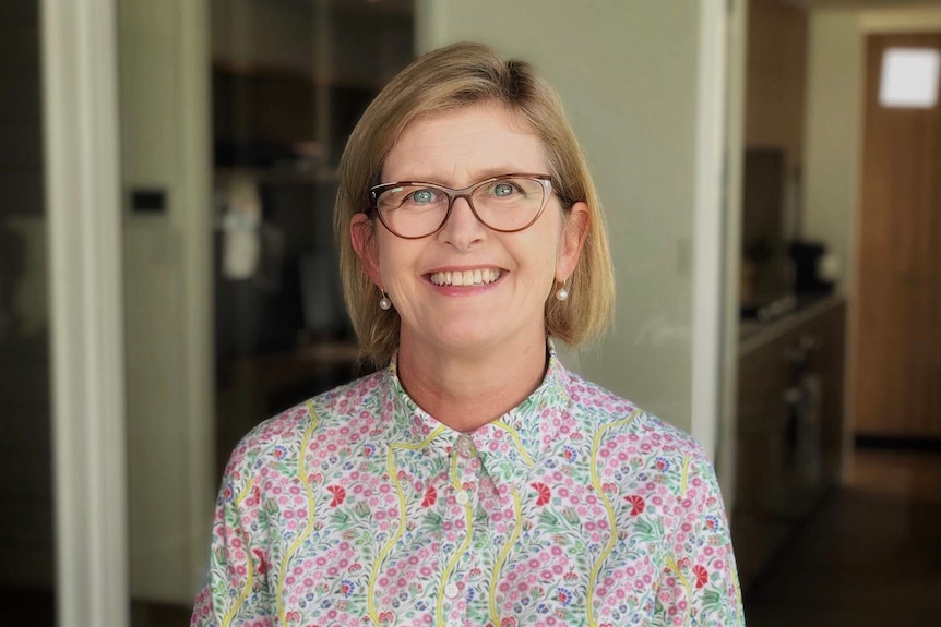 A woman wearing glasses and a floral shirt smiles at the camera.