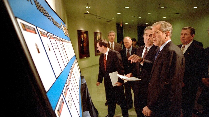 Robert Mueller (left) and George W. Bush (right) reviewing the list of the Most Wanted Terrorists on a notice board.
