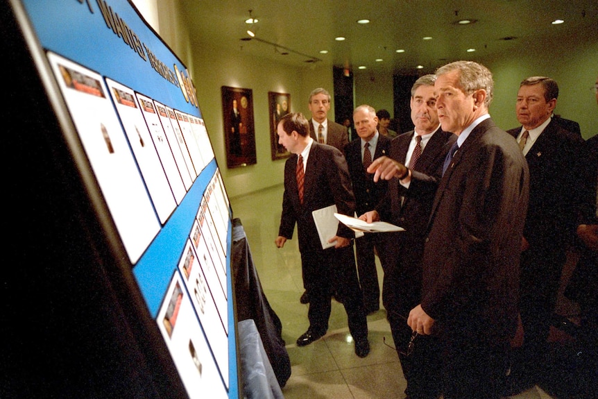 Robert Mueller (left) and George W. Bush (right) reviewing the list of the Most Wanted Terrorists on a notice board.