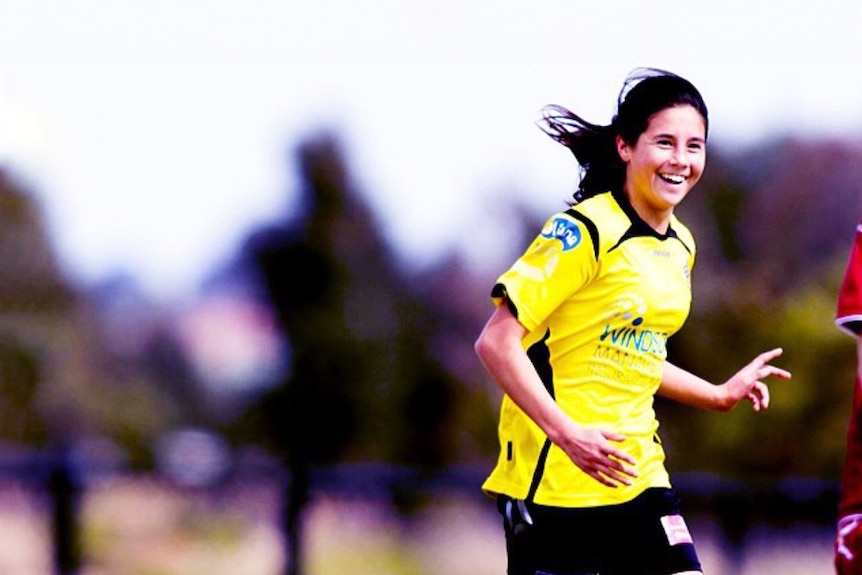 A teenage Kyra Cooney-Cross smiles and runs on a soccer field. She wears a yellow jersey, black shorts and yellow socks.