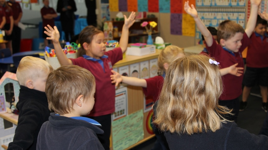 Primary school students stand in a classroom with their eyes closed and arms stretched out, practising mindfulness.