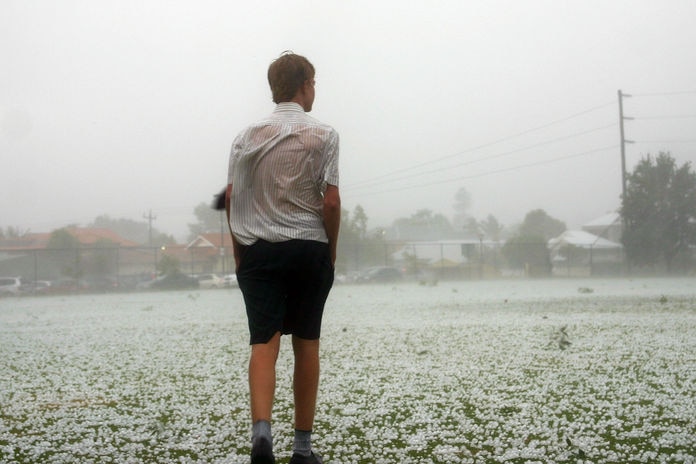 A boy stands in the middle of a playing field covered in hailstones.