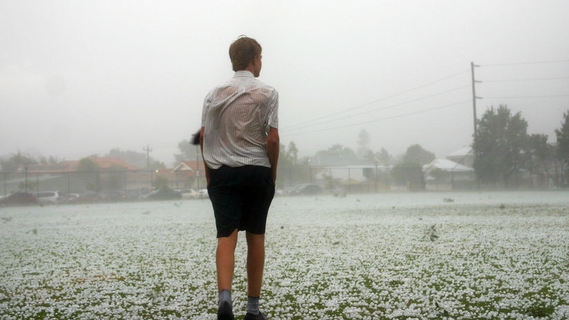 A boy stands in the middle of a playing field covered in hailstones.