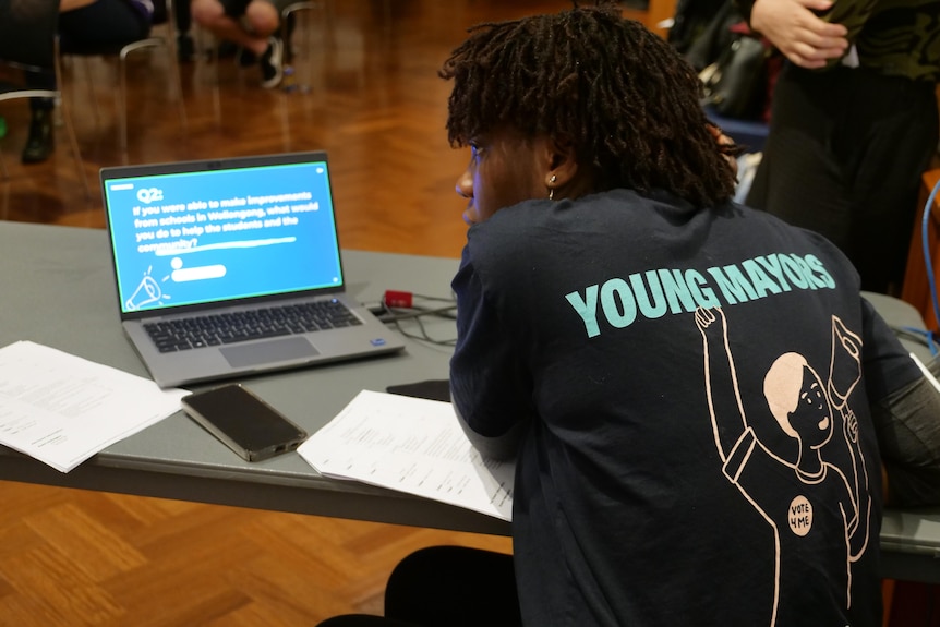 Back of YFA staff members shirt as she controls powerpoint at forum
