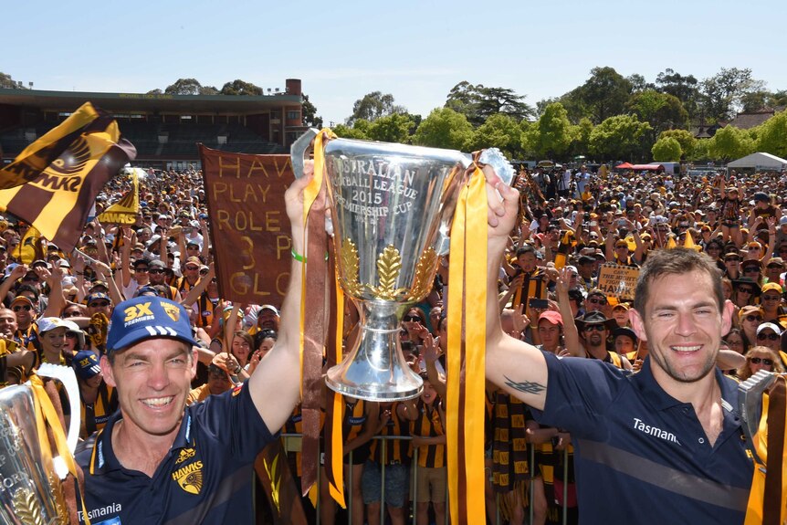Hawthorn coach Alastair Clarkson (L) and captain Luke Hodge hold up three AFL trophies in 2015.