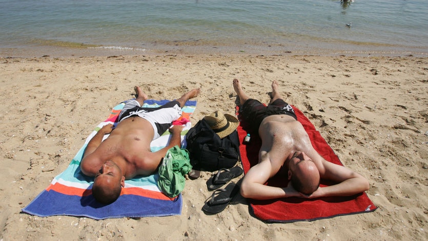 Two men lie on towels sunbaking at South Melbourne beach.