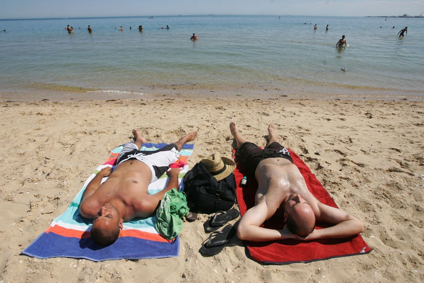 Two men lie on towels sunbaking at South Melbourne beach.