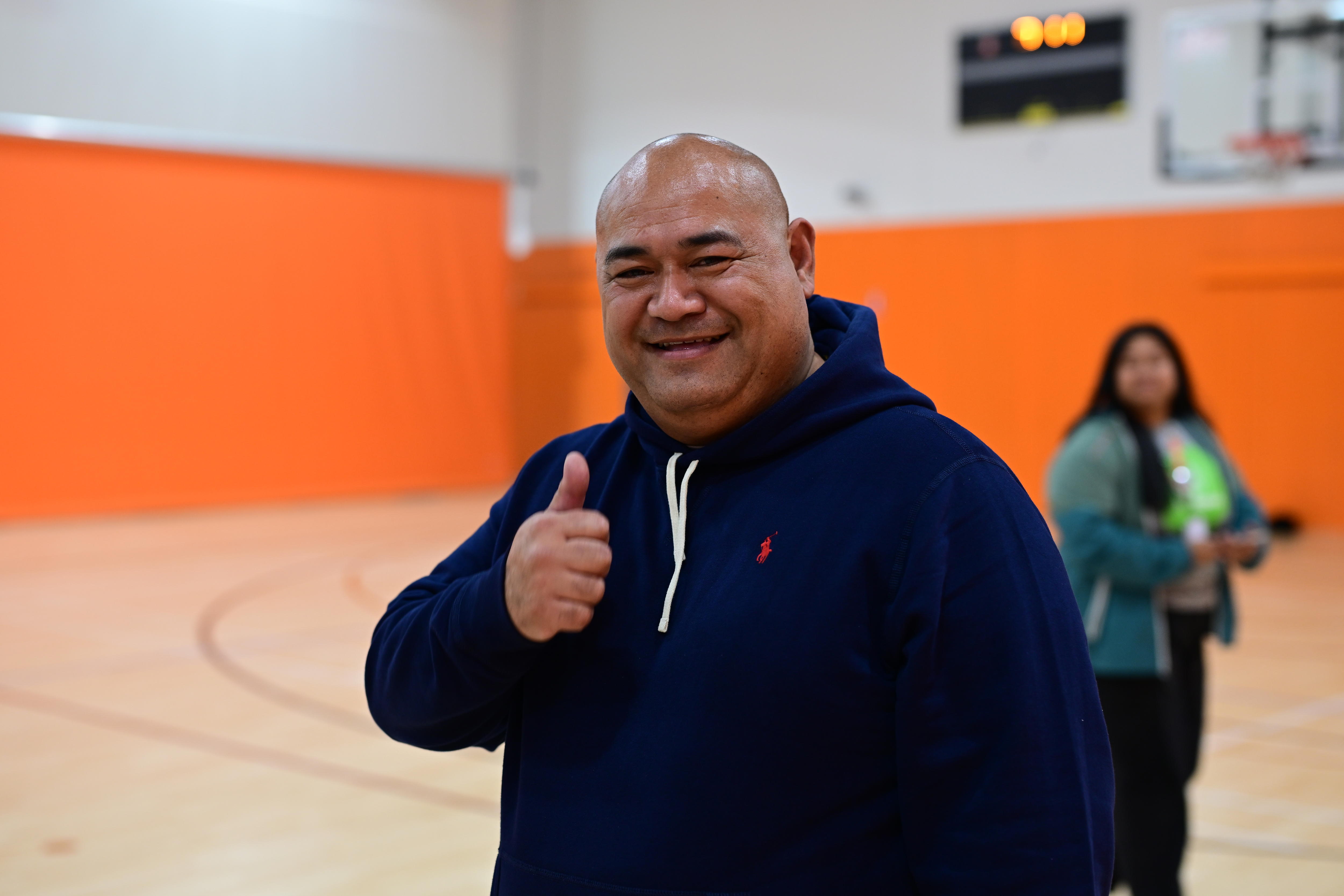A man standing on a basketball court gives the thumbs-up signal.