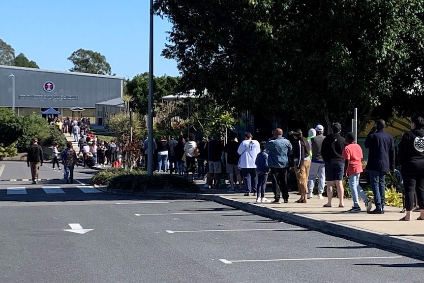 A long queue of people along a footpath running along a driveway leading to a building school building