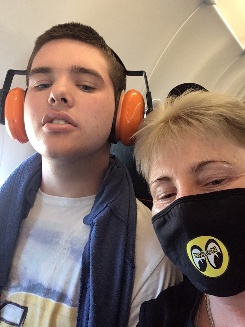 Boy with orange headphones while lady with black mask next to him.