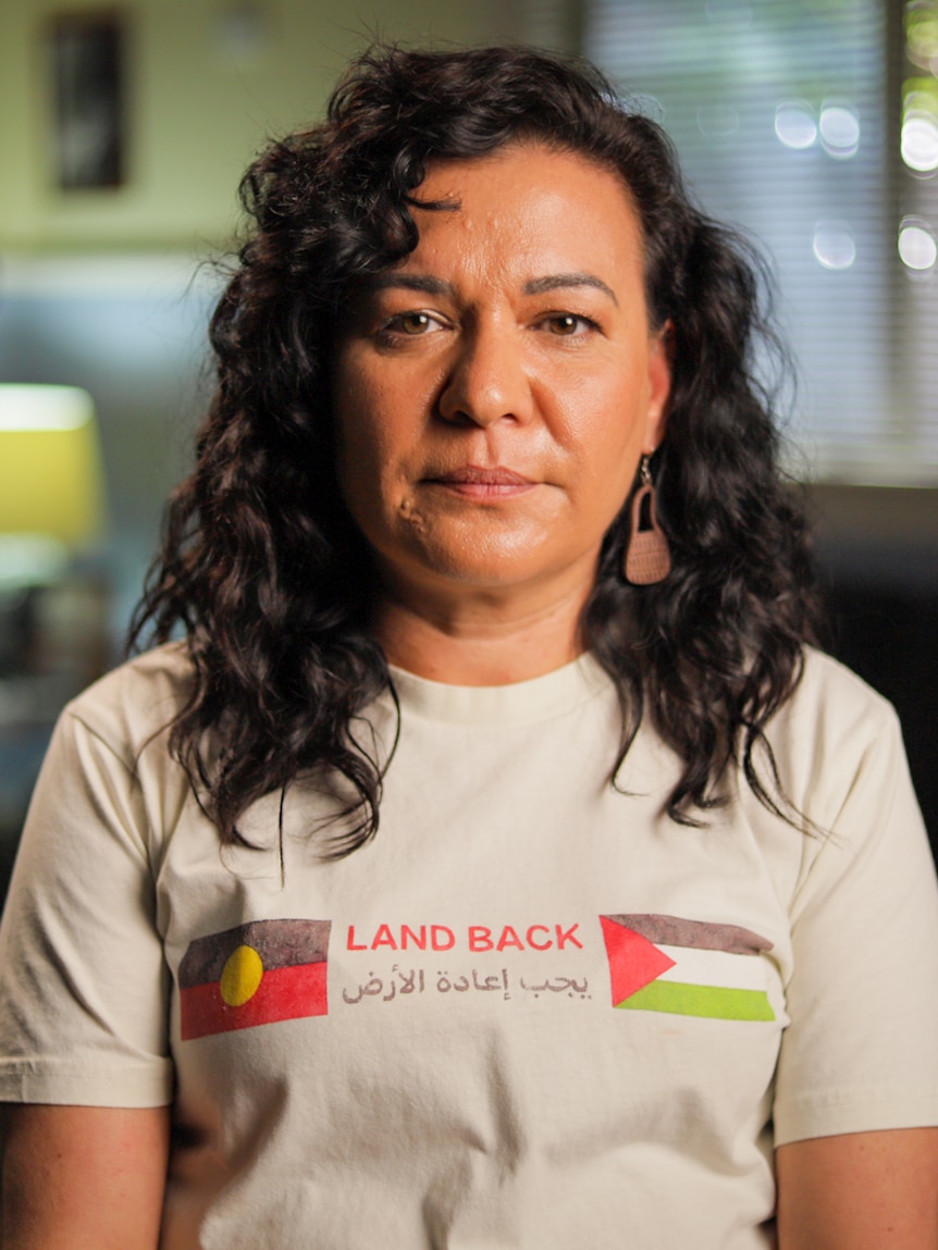 Woman wearing a white shirt with Aboriginal flag and Palestinian flag with the text, 'Land Back'.