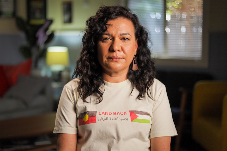 Woman wearing a white shirt with Aboriginal flag and Palestinian flag with the text, 'Land Back'.