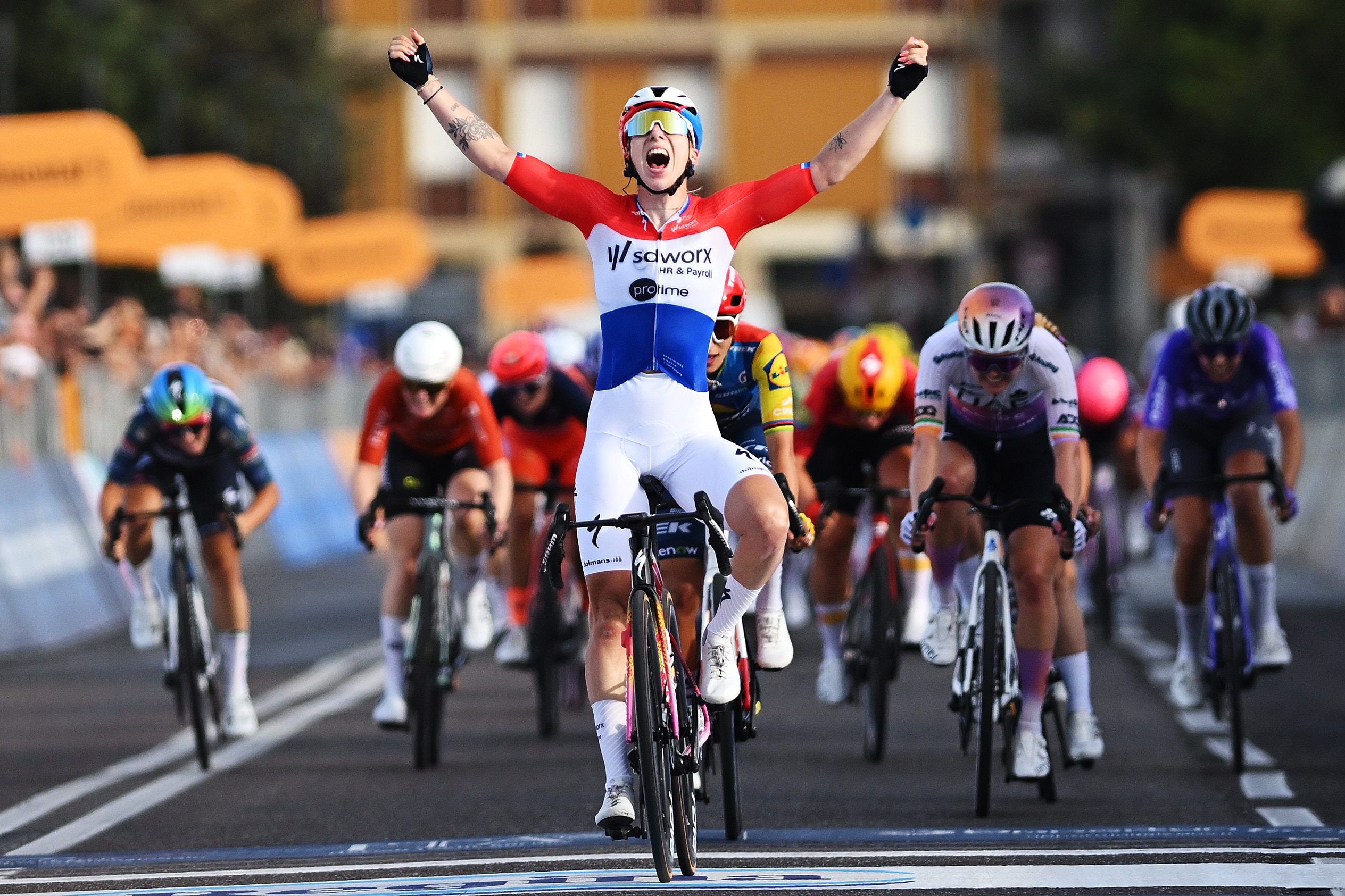 Lorena Wiebes holds up her hands in victory while cycling.