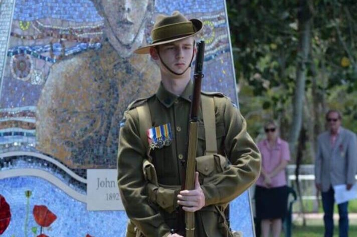A young man stands in front of a war memorial in an army uniform