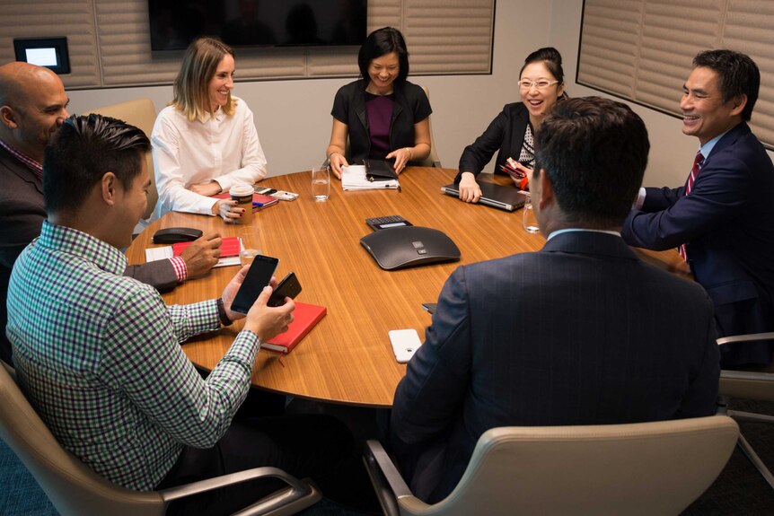 Seven people smile as they sit around a desk in a Sydney bank's meeting room.