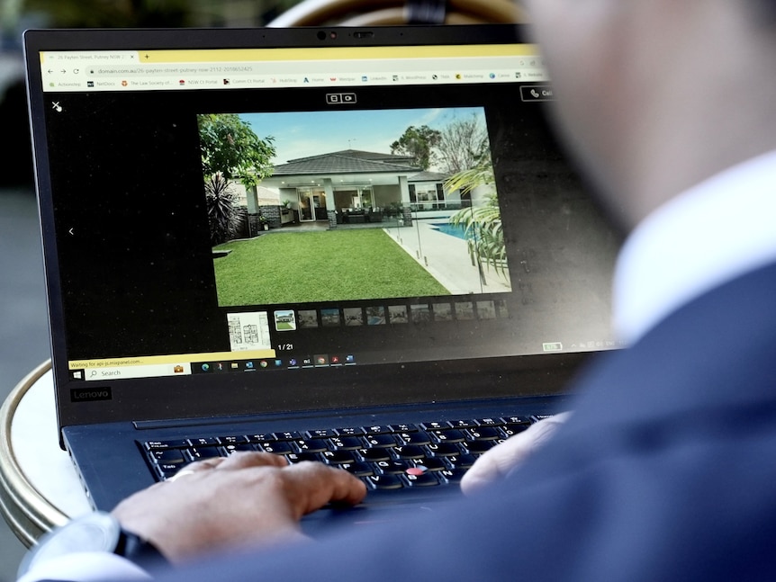 A man in a suit on a laptop searching real estate websites.