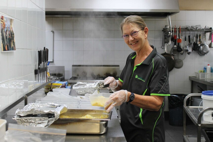 A woman cooking in an industrial kitchen smiles at the camera.