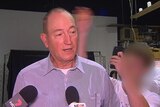 Fraser Anning speaks to the media, with a blurred image of a teenager seen in the background behind him.