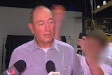 Fraser Anning speaks to the media, with a blurred image of a teenager seen in the background behind him.