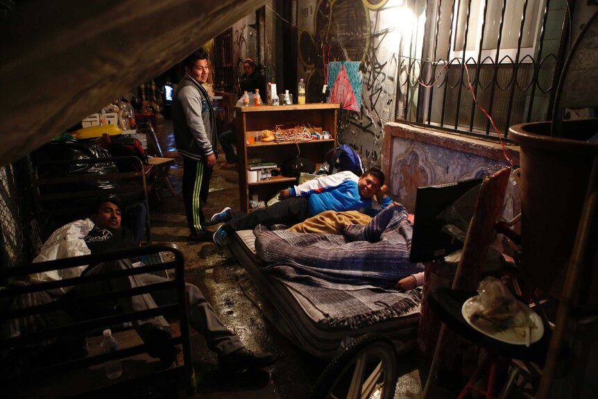 A family prepares to sleep under tarps on the sidewalk after their home was damaged.