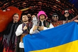 Winners of Eurovision 2022. Man with pink hat surrounded by other men on the Eurovision TV set.