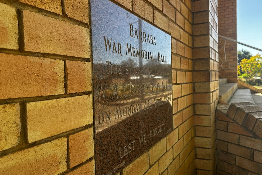 A close up of a gold plaque on a brick wall, reading Barraba War Memorial Hall.