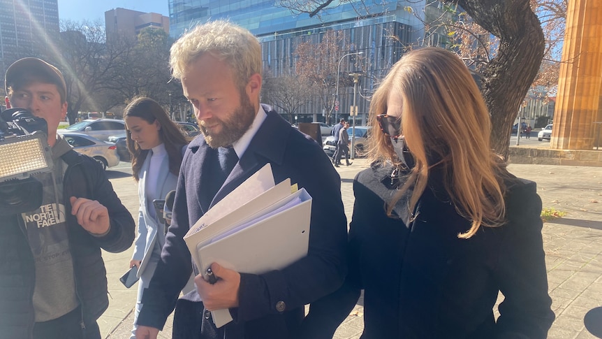 A woman in a black coat walking next to a man with a beard holding documents