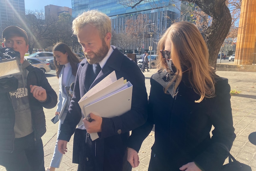 A woman in a black coat walking next to a man with a beard holding documents