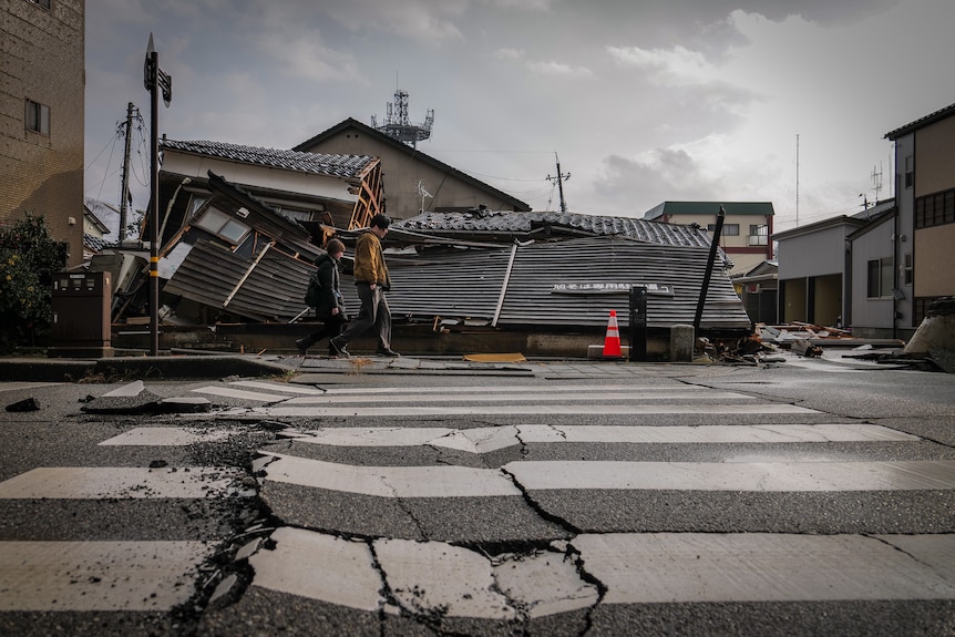 Image of a pedestrian crossing with large cracks, behind it are damaged houses.