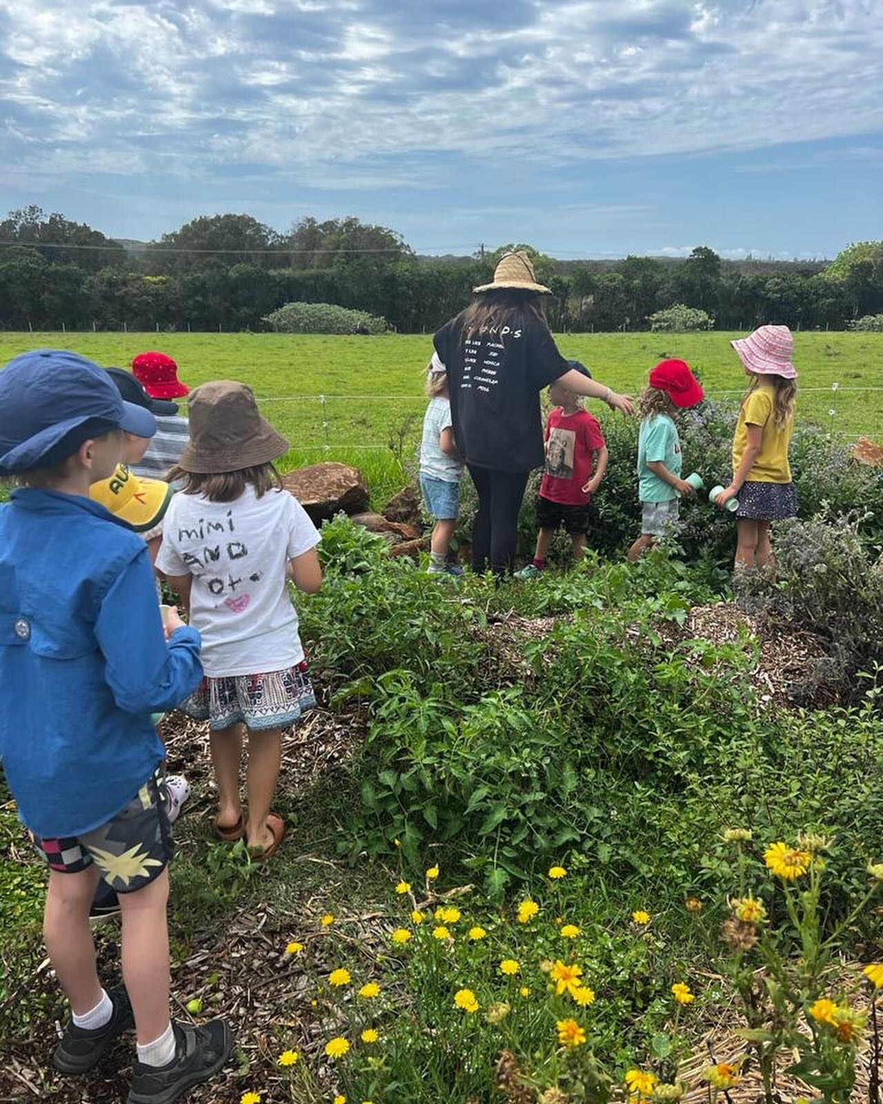 Niños y una mujer con sombreros recogen verduras en una granja.