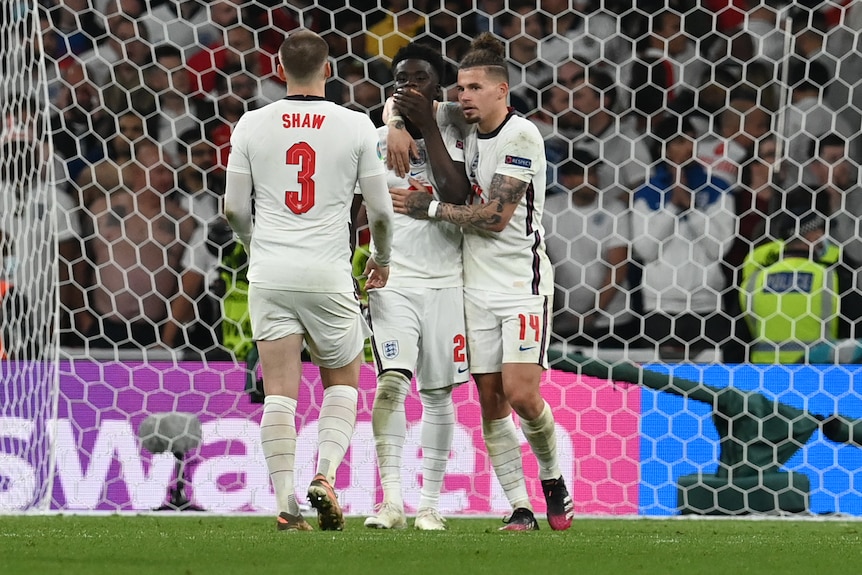 Bukayo Saka holds his hand to his mouth and is hugged by Kalvin Phillips