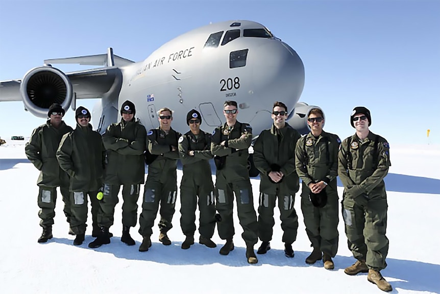 A crowd of men stand on the ice in front of an Air Force plan