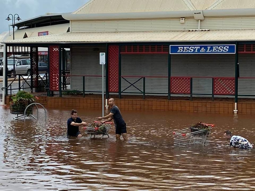 Three men knee-deep in floodwater on the main street of Broome.