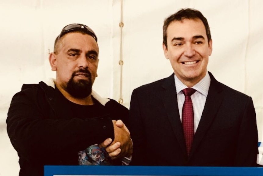 Two men shaking hands in front of lecturn with native title map and sign