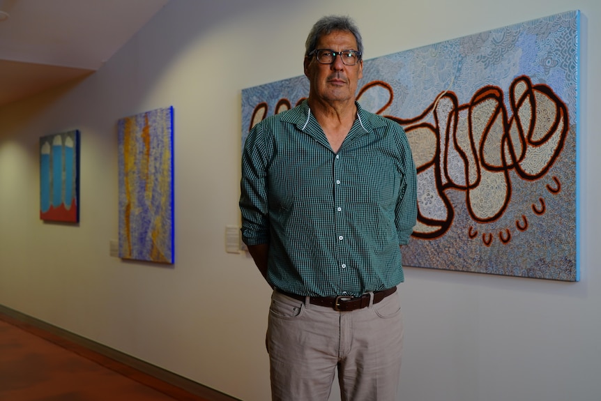 Man in green shirt, wearing glasses, stands in front of a blue painting