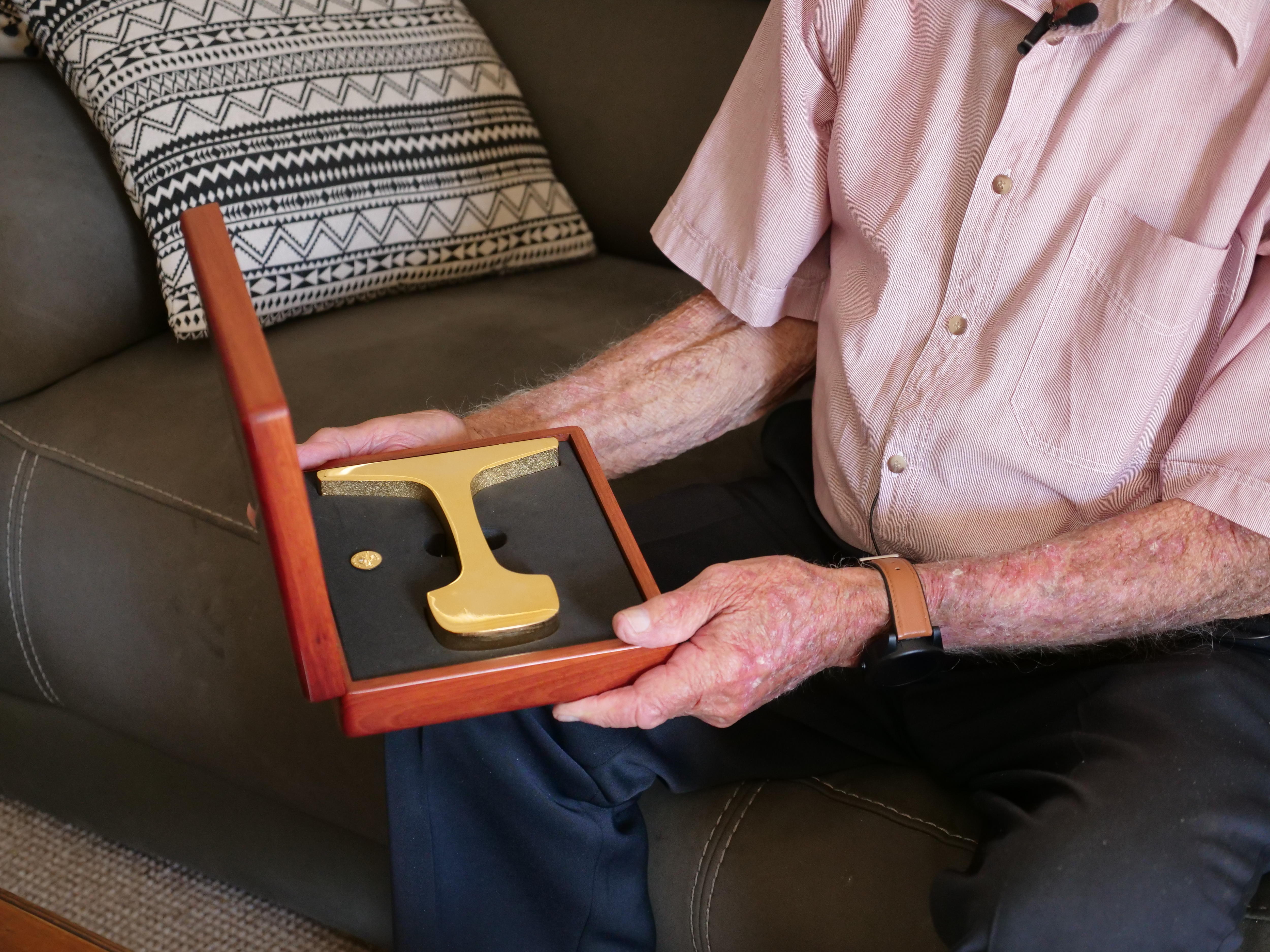 Uma caixa de madeira nas mãos de uma pessoa. Contém um pedaço de ferrovia dourada.