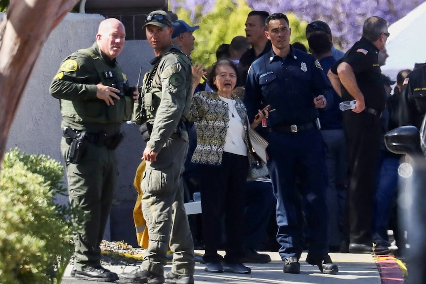 A woman speaks with law enforcement officers on a footpath.