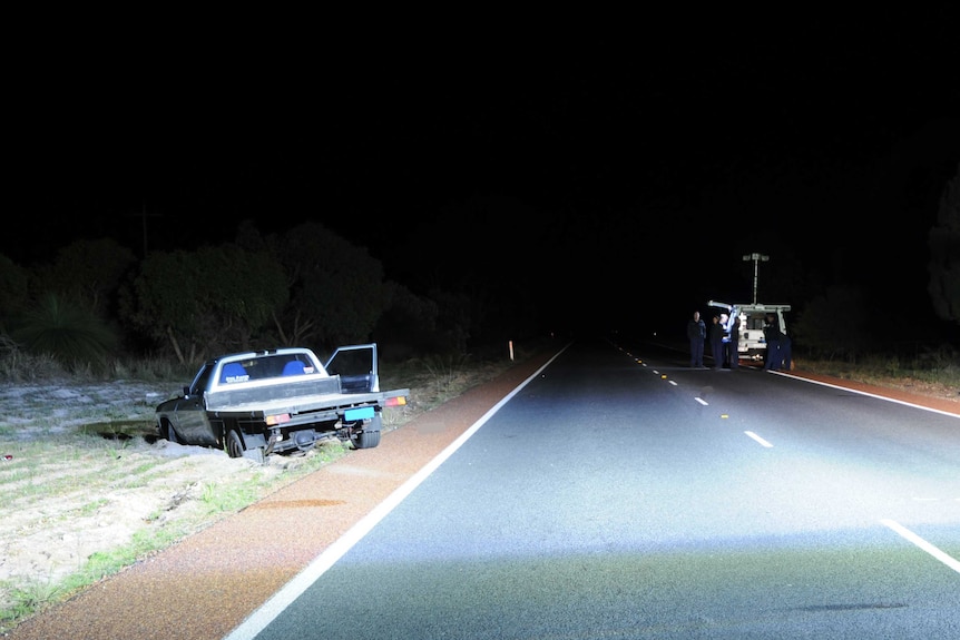 A vehicle lies bogged by the side of the road at night with a police car and officers on the opposite side of the road.