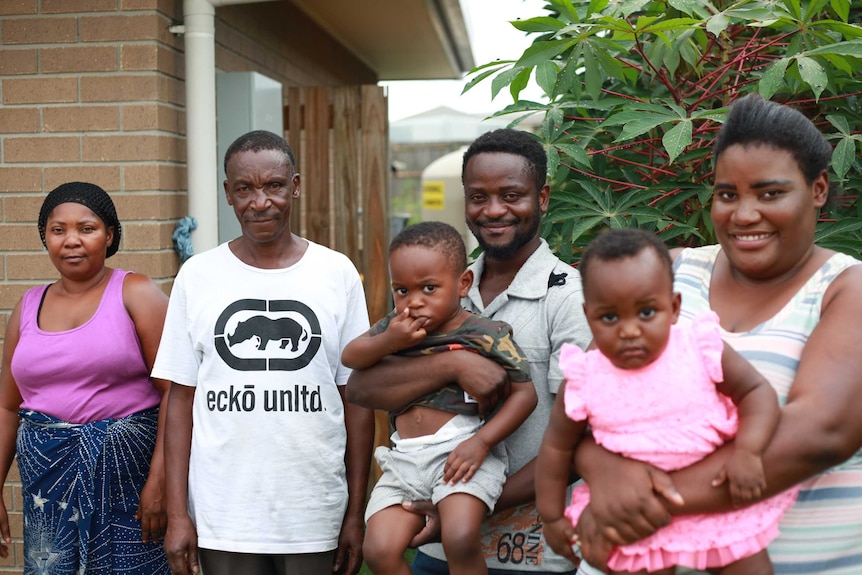 Jean Ntakarutimana stands in front of his house with his parents, wife and two children
