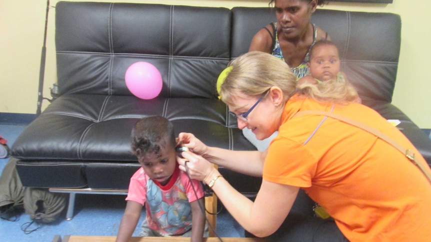Young indigenous child getting an ear check with parent watching on, audiologist in shot applying test