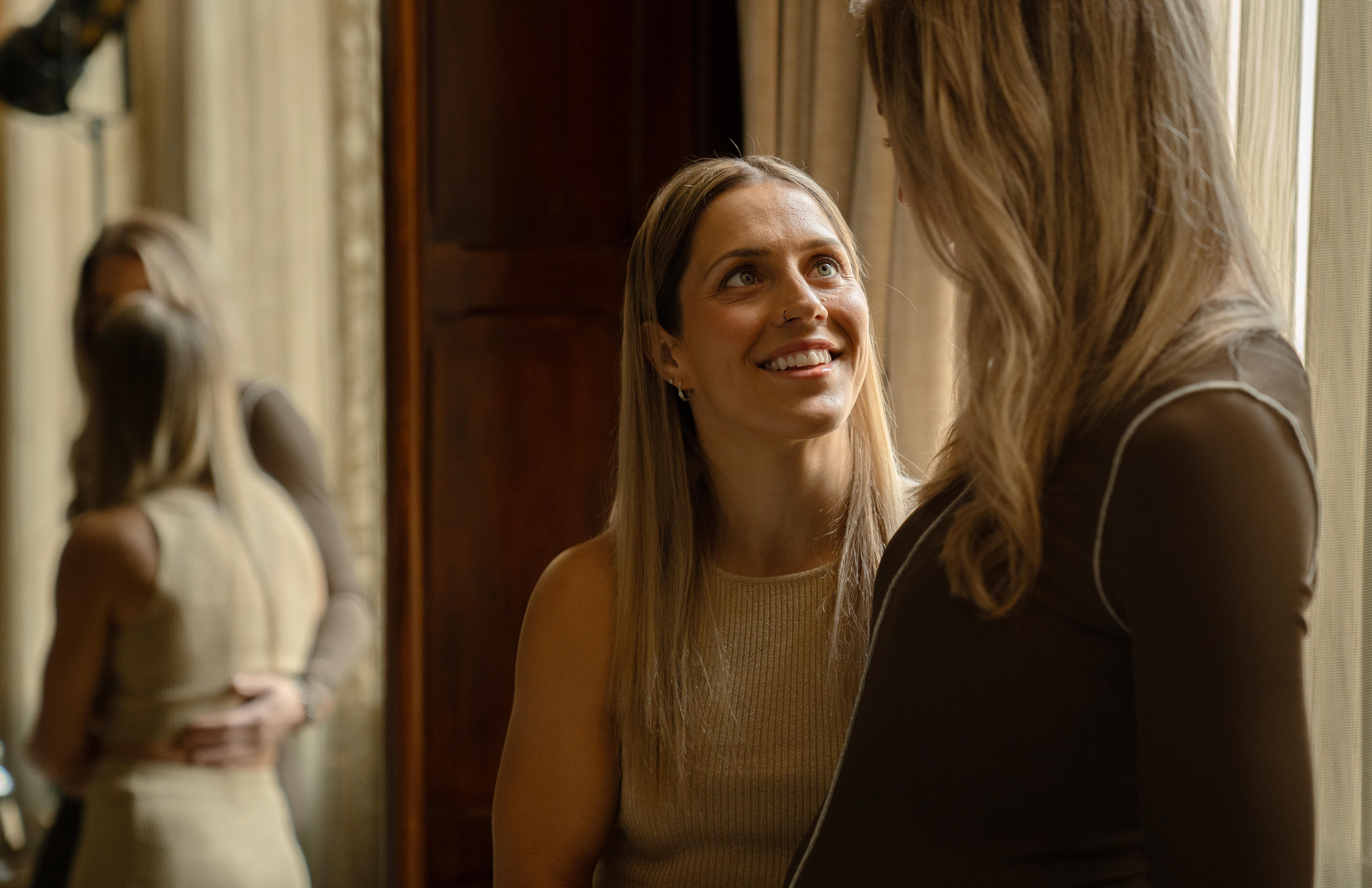 A blonde woman looks up smiling at another blonde woman