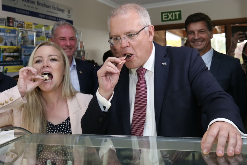 Scott Morrison and Jessica Whelan pose with ice cream sample sticks as a crowd watches from behind.