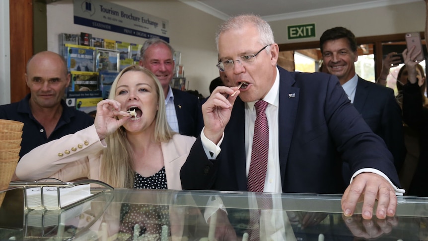Scott Morrison and Jessica Whelan pose with ice cream sample sticks as a crowd watches from behind.