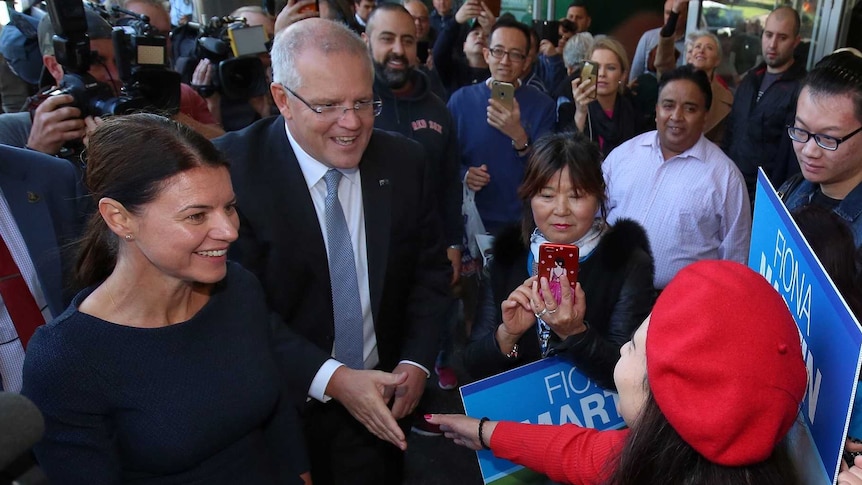 Scott Morrison shakes a woman's hand while surrounded by people as he walks down the street with Fiona Martin.