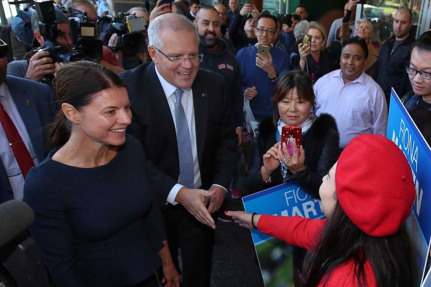 Scott Morrison shakes a woman's hand while surrounded by people as he walks down the street with Fiona Martin.