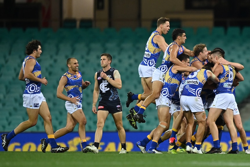 A group of West Coast AFL players leap on top of their teammate who has just kicked a long goal.