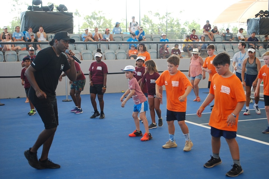 Baker Boy stands up the front with a microphone while a group copy his moves