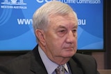 A headshot of John McKechnie in a suit in front of a CCC sign at a press conference.