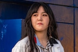 A woman sits at a park wearing a white jacket.