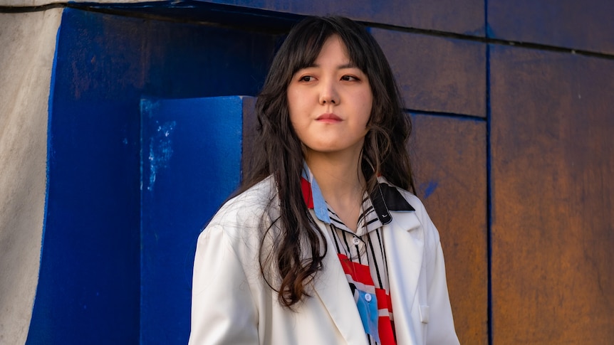 A woman sits at a park wearing a white jacket.